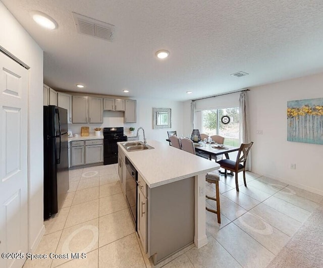 kitchen with a textured ceiling, black appliances, sink, gray cabinets, and a kitchen island with sink