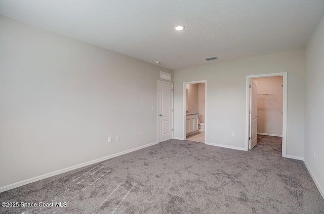 unfurnished bedroom featuring ensuite bath, a closet, light colored carpet, a textured ceiling, and a walk in closet