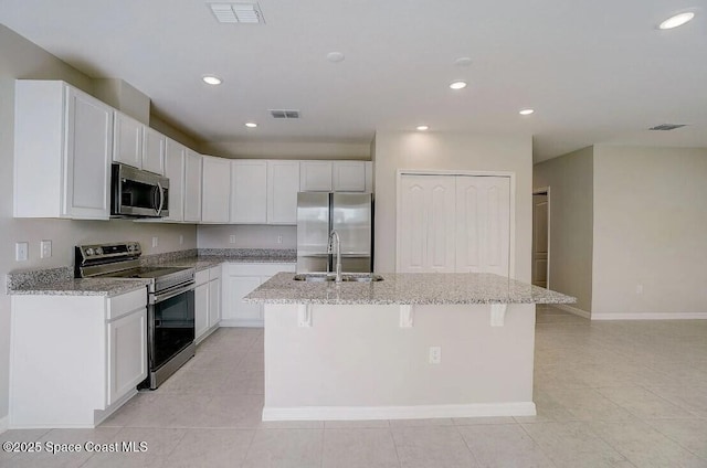 kitchen featuring light stone counters, white cabinets, appliances with stainless steel finishes, and a center island with sink