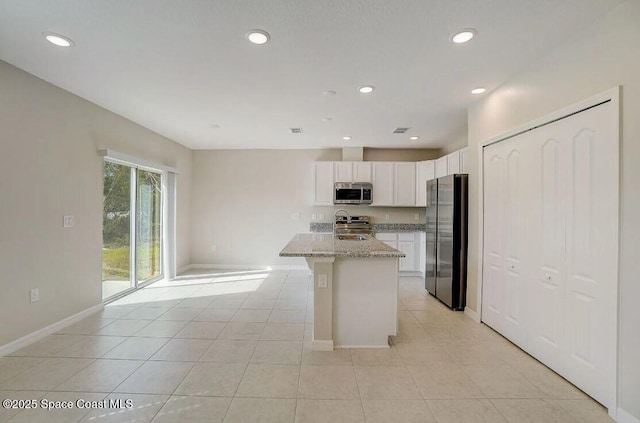 kitchen featuring white cabinetry, a kitchen island with sink, appliances with stainless steel finishes, light tile patterned floors, and light stone counters