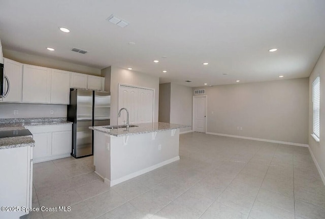 kitchen featuring white cabinetry, appliances with stainless steel finishes, a kitchen island with sink, light stone countertops, and sink