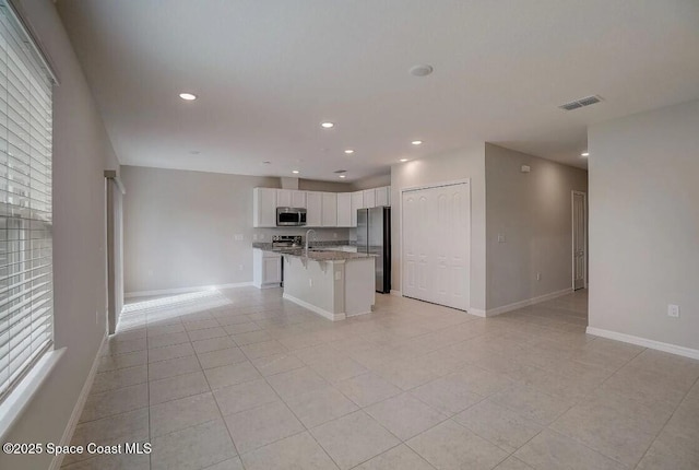 kitchen with white cabinets, stainless steel appliances, a kitchen island with sink, a breakfast bar, and light tile patterned floors