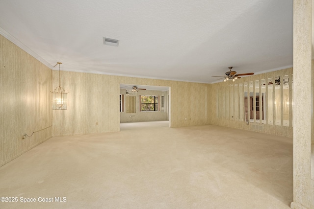 carpeted spare room featuring ceiling fan with notable chandelier and ornamental molding