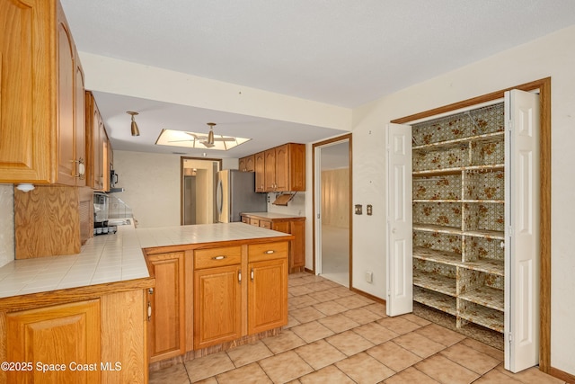 kitchen featuring stainless steel refrigerator, tile countertops, a skylight, and light tile patterned flooring