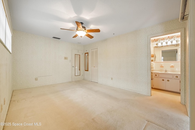 unfurnished bedroom featuring ensuite bathroom, sink, light colored carpet, and ceiling fan