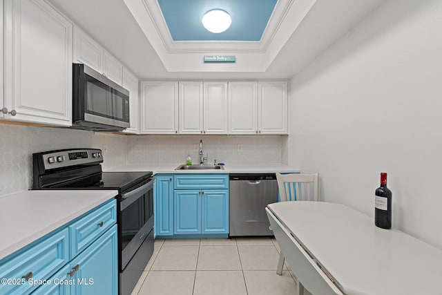 kitchen with appliances with stainless steel finishes, a raised ceiling, blue cabinets, crown molding, and sink