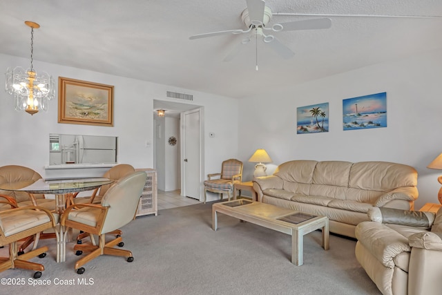 carpeted living area with ceiling fan with notable chandelier and visible vents