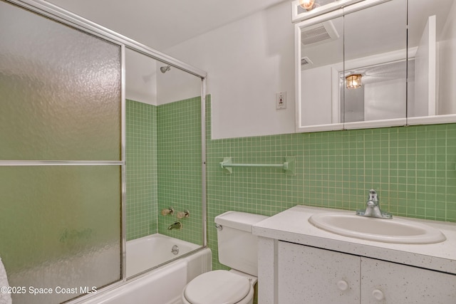 bathroom featuring toilet, shower / bath combination with glass door, visible vents, vanity, and tile walls