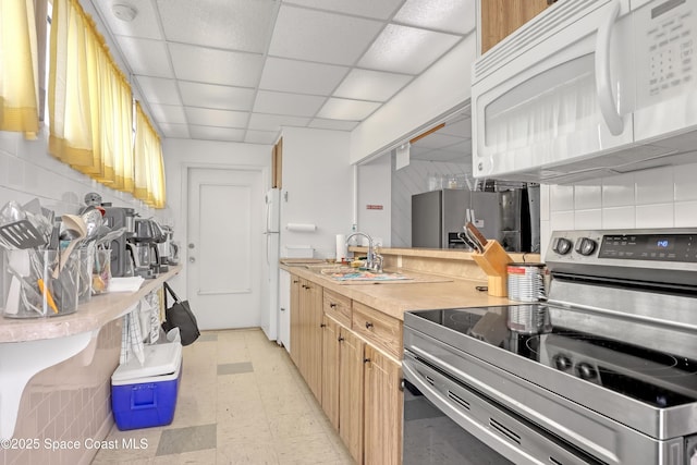 kitchen with a paneled ceiling, a sink, light countertops, appliances with stainless steel finishes, and light floors