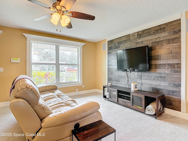 living room featuring a textured ceiling, light hardwood / wood-style flooring, ceiling fan, and wood walls