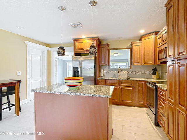 kitchen featuring sink, stainless steel appliances, light stone counters, a kitchen island, and decorative light fixtures