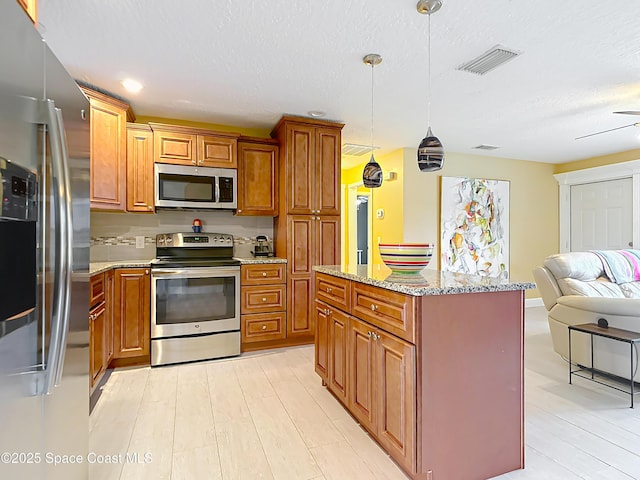 kitchen with pendant lighting, appliances with stainless steel finishes, tasteful backsplash, light stone countertops, and a textured ceiling