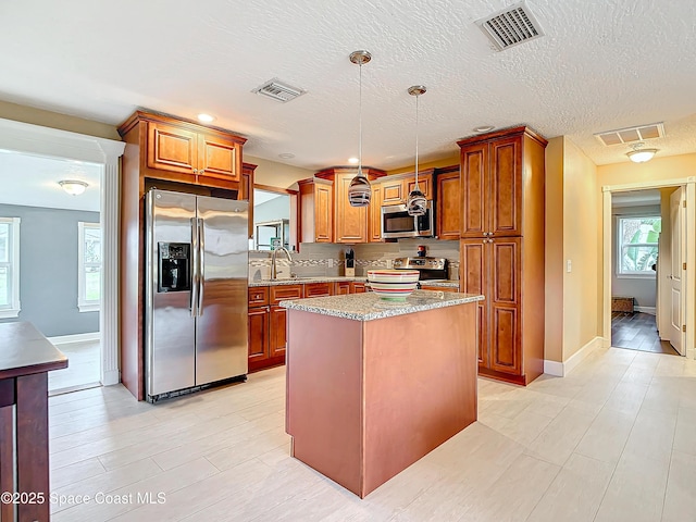 kitchen featuring sink, appliances with stainless steel finishes, a center island, light stone counters, and decorative light fixtures