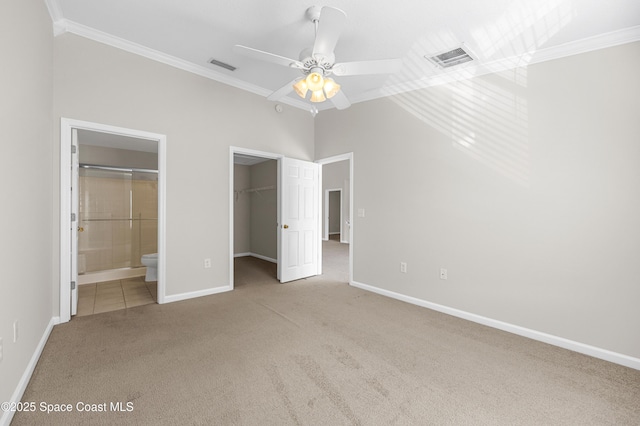 unfurnished bedroom with ceiling fan, connected bathroom, ornamental molding, a walk in closet, and light colored carpet