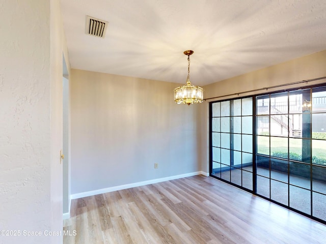 empty room featuring light wood-type flooring and a notable chandelier