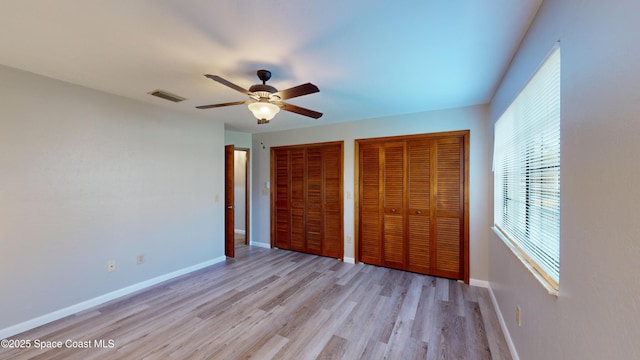 unfurnished bedroom featuring ceiling fan, light hardwood / wood-style flooring, and multiple closets