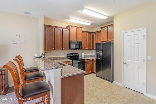 kitchen featuring black appliances, kitchen peninsula, sink, a kitchen breakfast bar, and dark stone counters