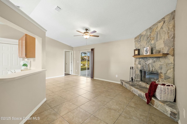 unfurnished living room featuring a stone fireplace, vaulted ceiling, a textured ceiling, light tile patterned floors, and ceiling fan