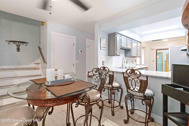 kitchen with kitchen peninsula, decorative backsplash, gray cabinetry, light tile patterned flooring, and sink