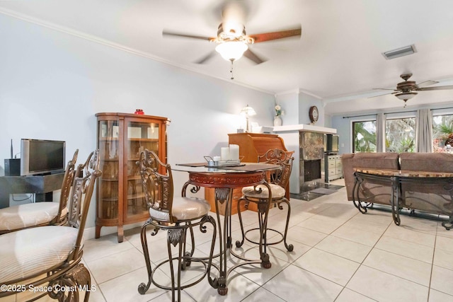 dining room featuring ceiling fan, light tile patterned flooring, crown molding, and a fireplace