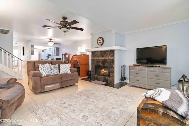 living room with ceiling fan, light tile patterned flooring, crown molding, and a tile fireplace