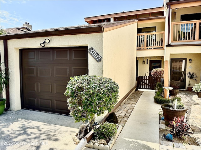 view of exterior entry featuring a balcony, an attached garage, concrete driveway, and stucco siding