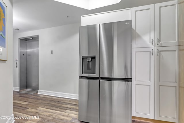 kitchen with light hardwood / wood-style flooring, stainless steel fridge, white cabinetry, and elevator