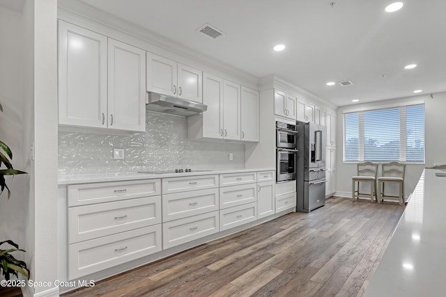 kitchen with tasteful backsplash, white cabinets, appliances with stainless steel finishes, and light hardwood / wood-style flooring