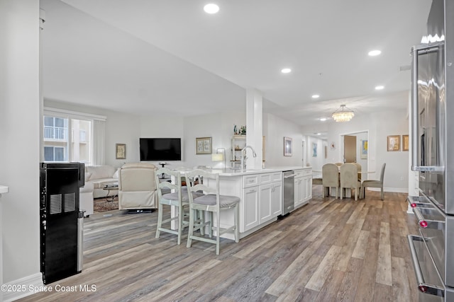 kitchen featuring light hardwood / wood-style floors, pendant lighting, a center island with sink, high quality fridge, and white cabinetry