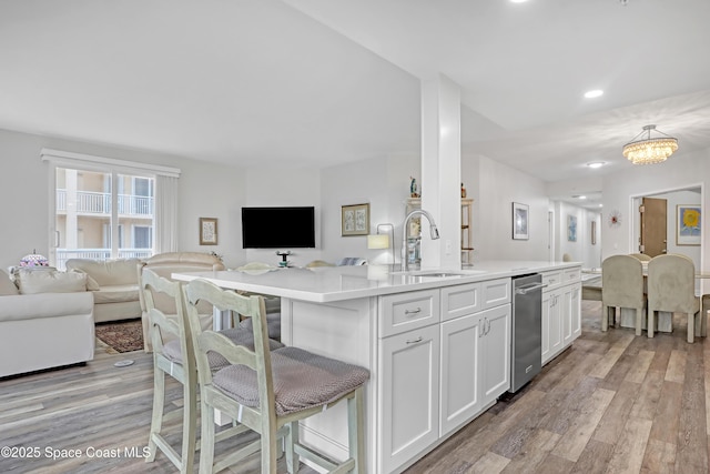 kitchen featuring white cabinetry, a kitchen island with sink, light wood-type flooring, decorative light fixtures, and sink