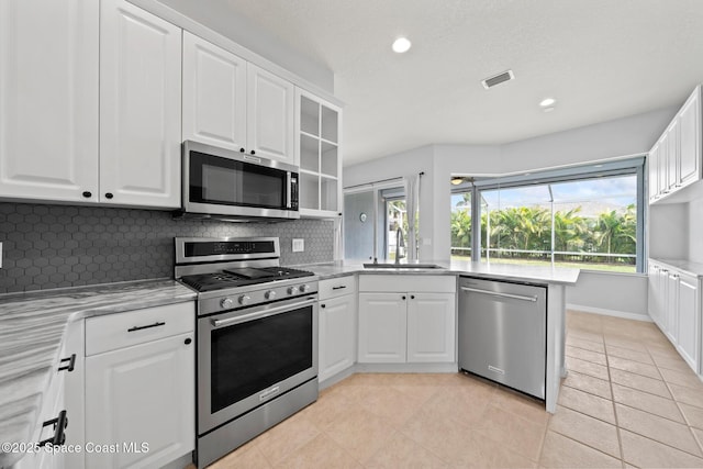 kitchen with light tile patterned flooring, kitchen peninsula, appliances with stainless steel finishes, and white cabinets