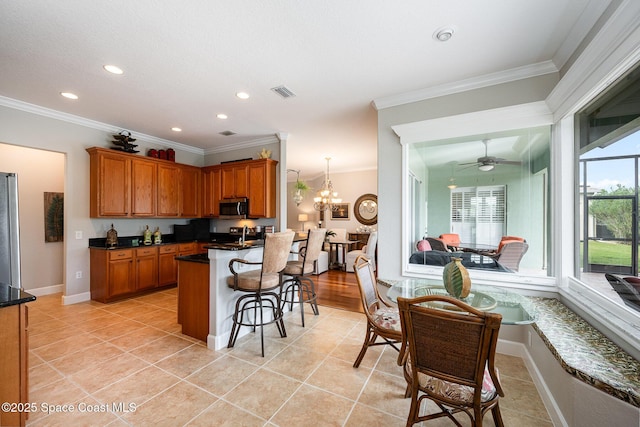 kitchen with ceiling fan with notable chandelier, a kitchen breakfast bar, hanging light fixtures, light tile patterned floors, and crown molding