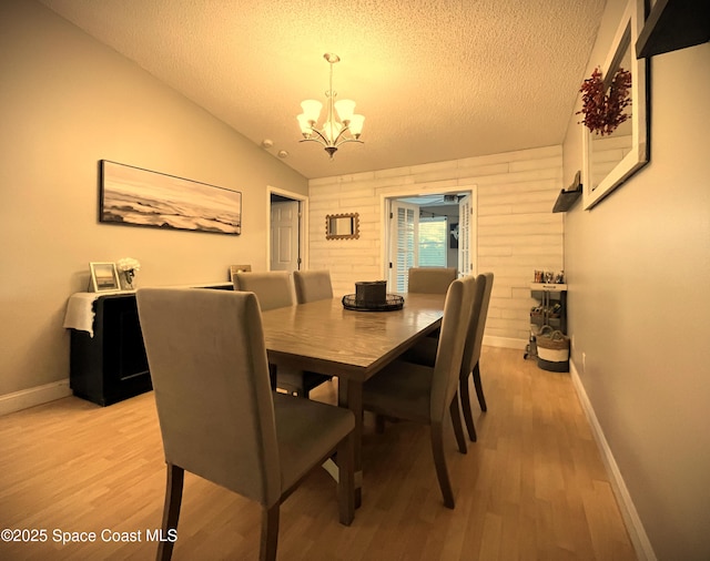 dining room with a notable chandelier, light hardwood / wood-style floors, a textured ceiling, and wood walls