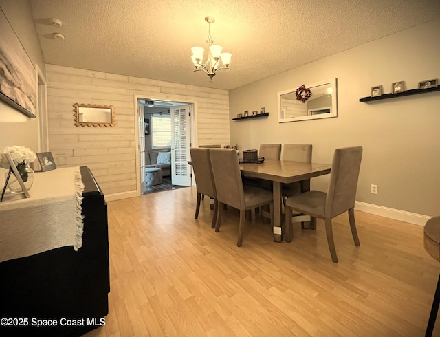 dining area with wooden walls, a chandelier, light hardwood / wood-style floors, and a textured ceiling