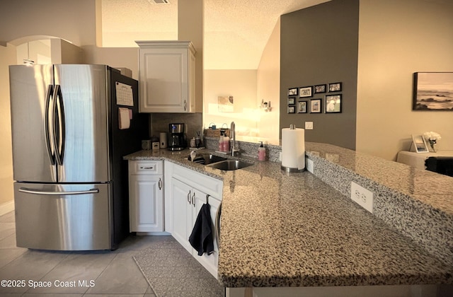 kitchen with sink, stainless steel fridge, white cabinetry, light stone countertops, and kitchen peninsula