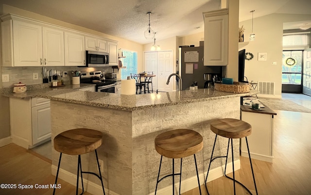 kitchen with stainless steel appliances, kitchen peninsula, vaulted ceiling, and white cabinets