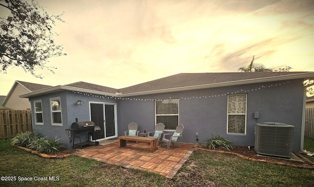 back house at dusk featuring a yard, a patio area, and central air condition unit