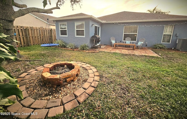 back house at dusk with central AC, a lawn, a patio area, and a fire pit