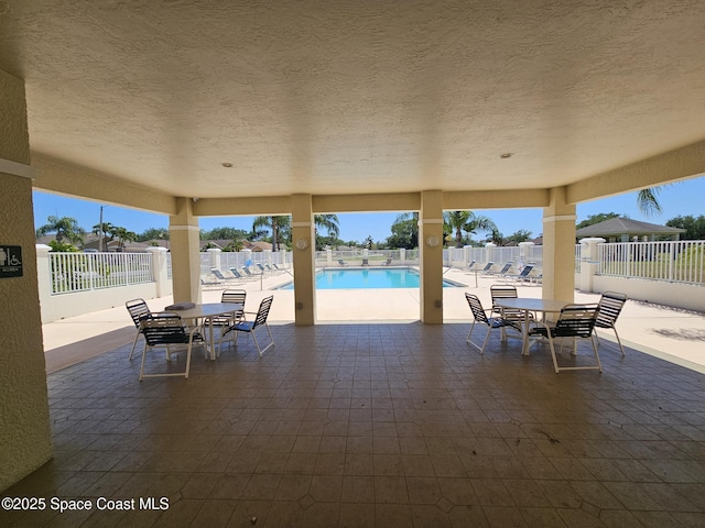 view of patio with a community pool, fence private yard, and outdoor dining area
