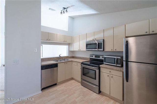 kitchen with appliances with stainless steel finishes, cream cabinetry, high vaulted ceiling, and sink