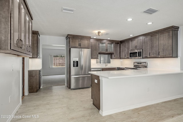 kitchen with appliances with stainless steel finishes, sink, dark brown cabinets, and light wood-type flooring