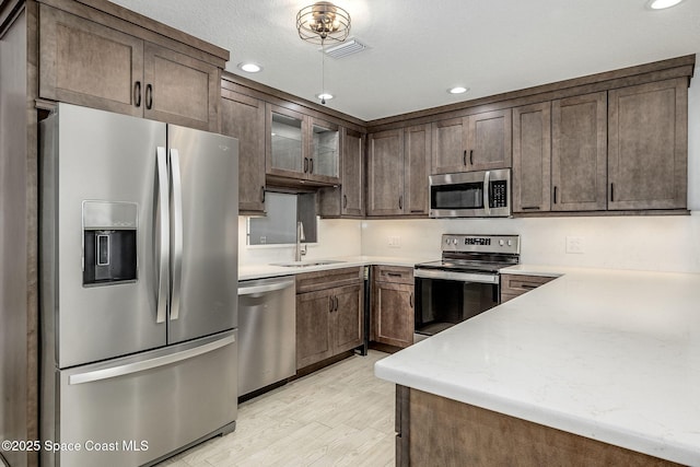 kitchen featuring appliances with stainless steel finishes, sink, light stone countertops, dark brown cabinets, and light hardwood / wood-style flooring