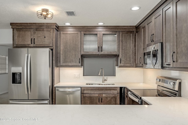 kitchen with appliances with stainless steel finishes, sink, a textured ceiling, and dark brown cabinetry