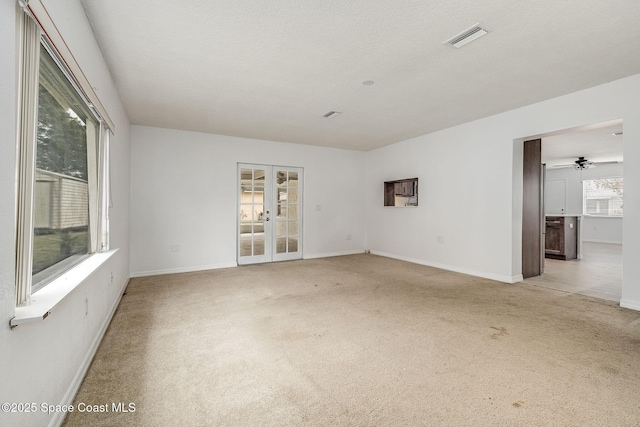 spare room featuring french doors, light colored carpet, and a textured ceiling