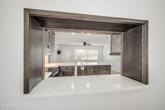 kitchen with stove, dark brown cabinets, kitchen peninsula, and ceiling fan