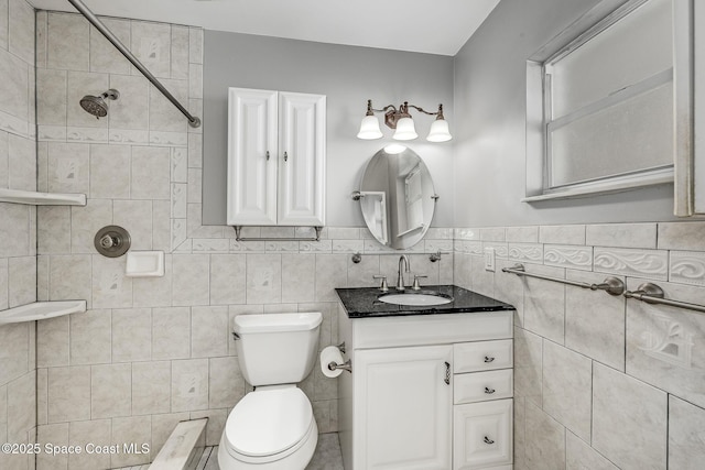 bathroom featuring vanity, a tile shower, tile walls, and toilet