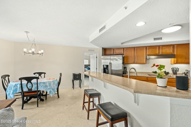 kitchen featuring decorative light fixtures, a textured ceiling, stainless steel fridge, and a kitchen bar