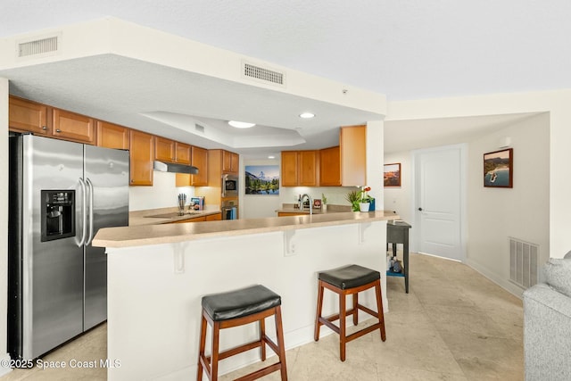 kitchen featuring appliances with stainless steel finishes, sink, a kitchen breakfast bar, kitchen peninsula, and a raised ceiling