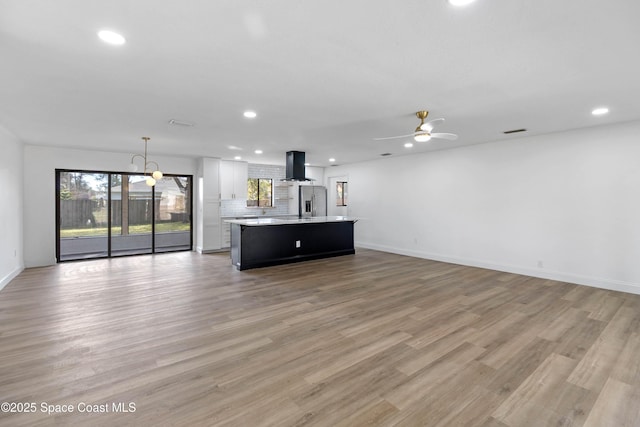 unfurnished living room with light wood-type flooring and ceiling fan with notable chandelier