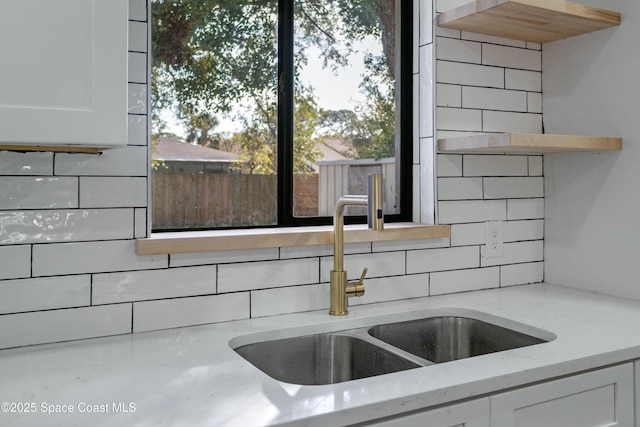 interior details featuring light stone counters, sink, white cabinets, and tasteful backsplash